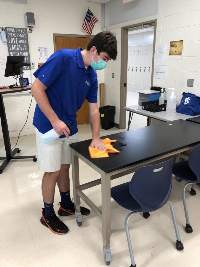 Quinn Walsh, 23, sanitizes a table in Mr. Bernings room