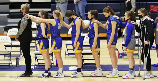 The girls varsity basketball team stands at attention during the national anthem prior to the game against Xavier.