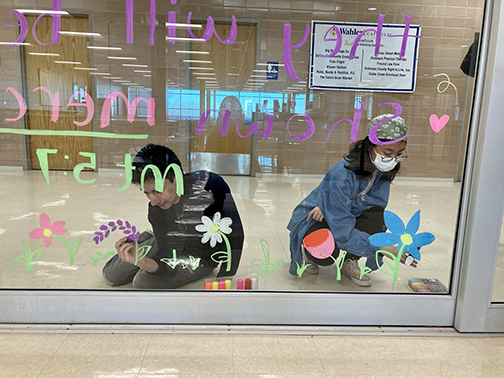 Beautifying the cafeteria windows are Marco Morel '22 and Marina Hishikawa '22 of Art Club. 